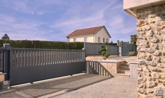 Image d'un portail coulissant 3m en aluminium gris anthracite installé devant une maison moderne.